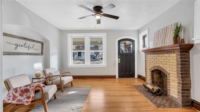 living area with a textured ceiling, a fireplace, wood finished floors, and baseboards