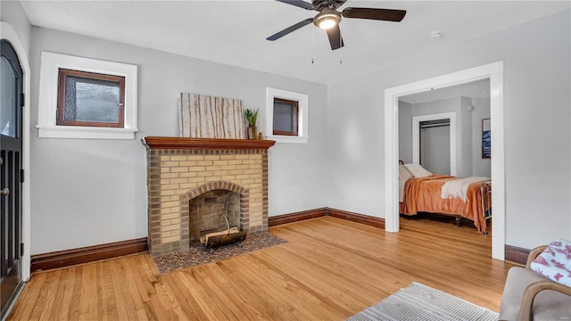 living area with a brick fireplace, a ceiling fan, baseboards, and wood finished floors