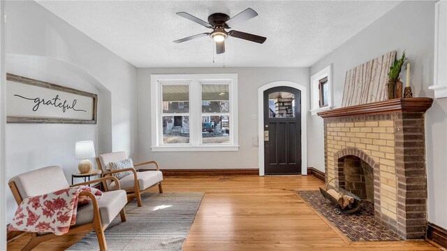 sitting room with a brick fireplace, a textured ceiling, baseboards, and wood finished floors