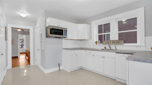 kitchen with stainless steel microwave, white cabinets, a sink, dishwasher, and baseboards