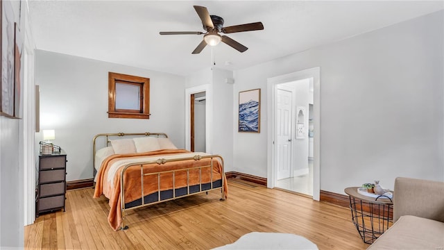 bedroom featuring light wood finished floors, ensuite bath, a ceiling fan, and baseboards