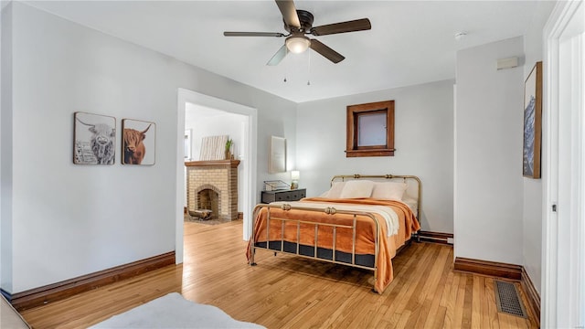 bedroom with ceiling fan, light wood-style flooring, visible vents, baseboards, and a brick fireplace