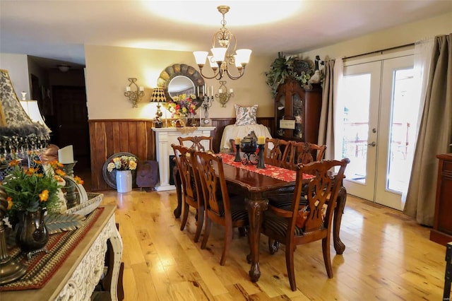 dining space with wooden walls, light hardwood / wood-style flooring, an inviting chandelier, and french doors