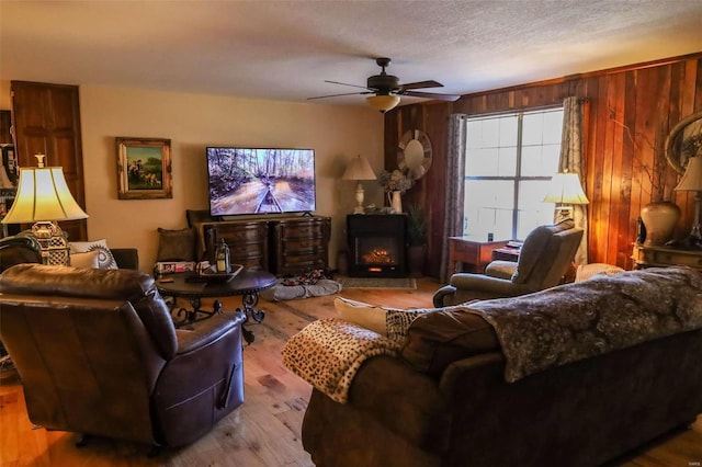 living room featuring a textured ceiling, wood walls, ceiling fan, and light hardwood / wood-style flooring