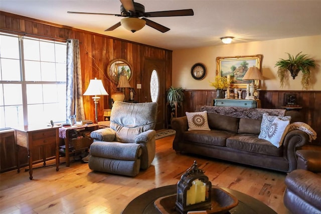 living room featuring ceiling fan, light hardwood / wood-style flooring, and wood walls