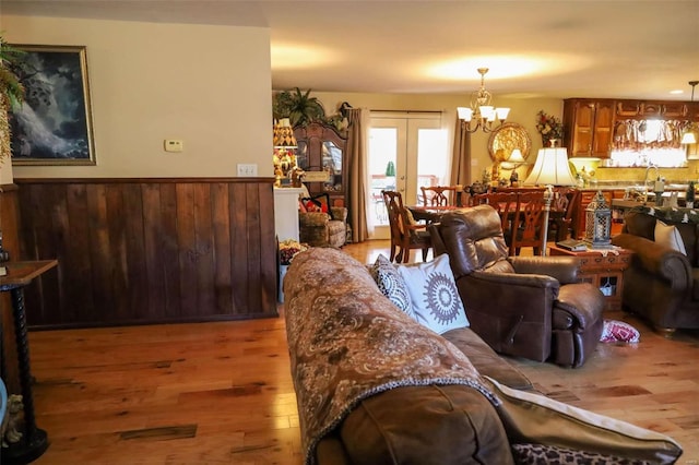 living room with french doors, wooden walls, a chandelier, and light hardwood / wood-style flooring