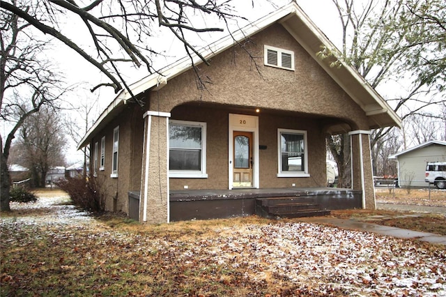 bungalow-style home with a porch, fence, and stucco siding