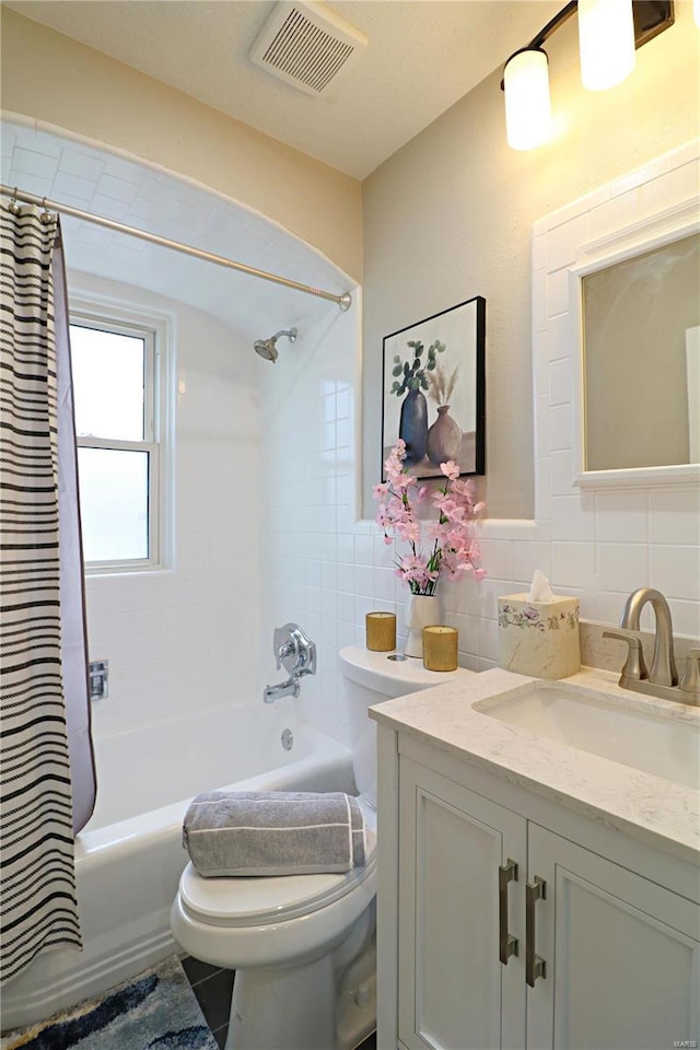 full bath featuring visible vents, shower / bath combo with shower curtain, toilet, and tile walls