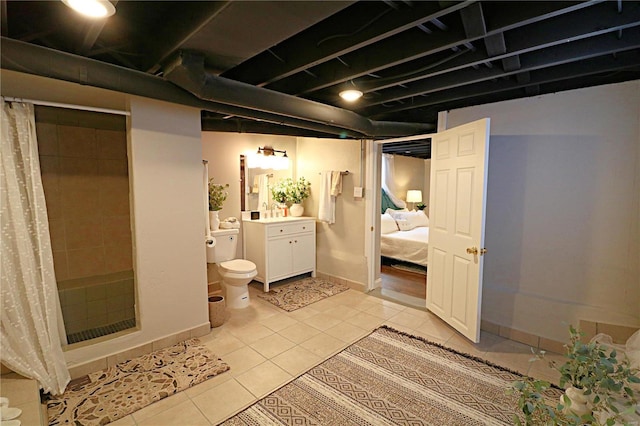 ensuite bathroom with tile patterned floors, toilet, a tile shower, baseboards, and vanity