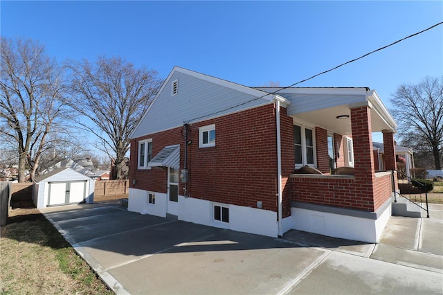 view of side of home featuring an outbuilding, fence, driveway, a storage shed, and brick siding