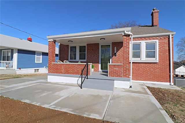 view of front of house with brick siding, covered porch, a chimney, and central AC