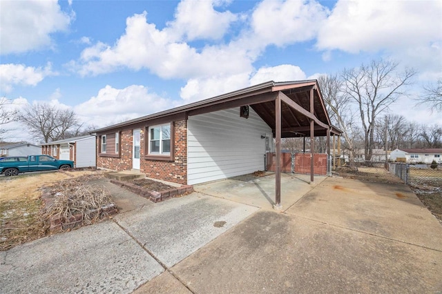 exterior space featuring an attached carport, concrete driveway, brick siding, and fence