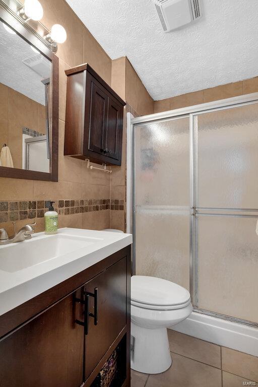 bathroom with tile walls, tile patterned floors, toilet, and a textured ceiling