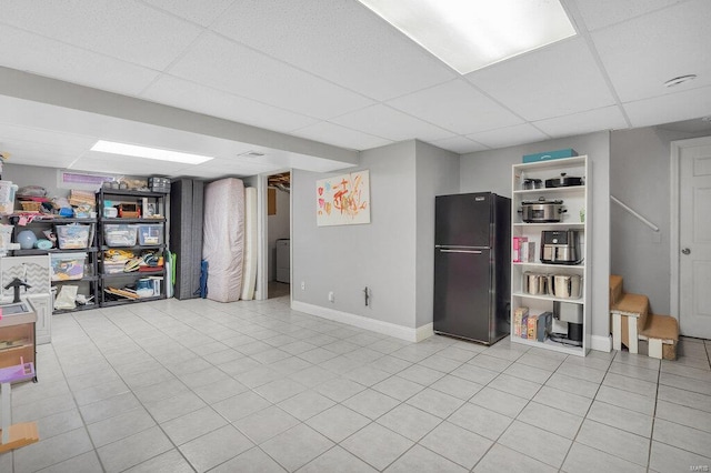 basement with black refrigerator, a paneled ceiling, and light tile patterned flooring