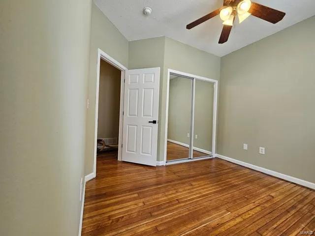 unfurnished bedroom featuring a ceiling fan, a closet, baseboards, and hardwood / wood-style flooring