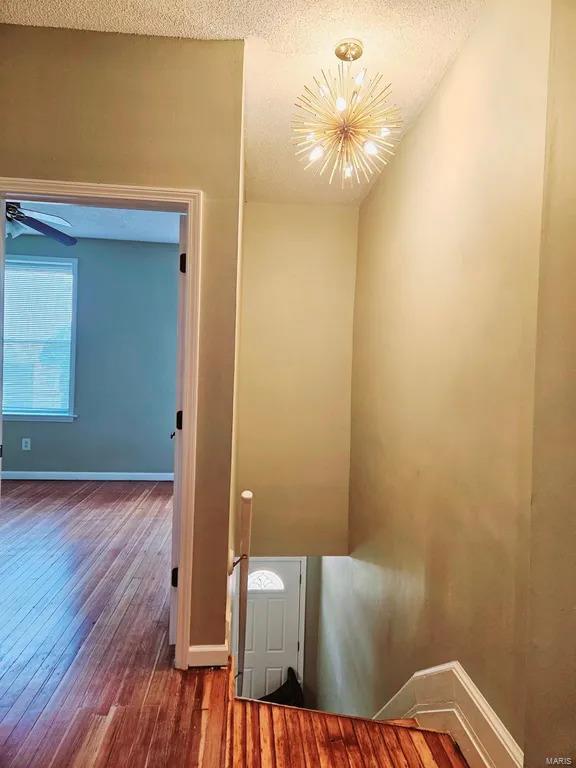 hallway featuring a textured ceiling, an inviting chandelier, wood finished floors, and baseboards