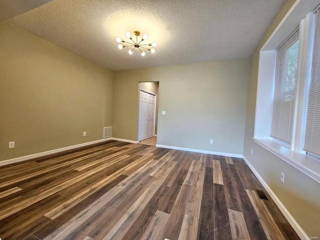 empty room featuring baseboards, visible vents, dark wood-style flooring, an inviting chandelier, and a textured ceiling