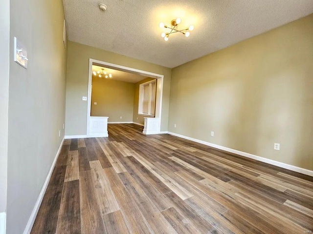 empty room featuring a textured ceiling, baseboards, a chandelier, and wood finished floors