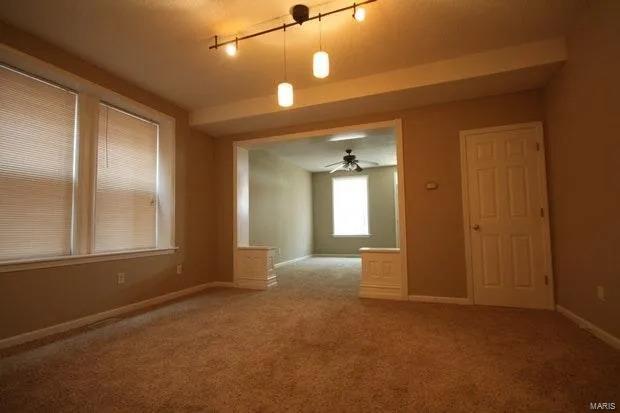 carpeted spare room featuring rail lighting, a ceiling fan, and baseboards