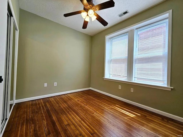 empty room with a textured ceiling, hardwood / wood-style flooring, visible vents, and baseboards