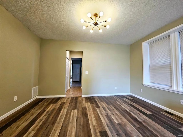 spare room with dark wood-type flooring, visible vents, baseboards, and an inviting chandelier