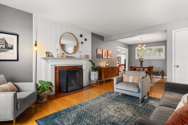 living room featuring a brick fireplace, a chandelier, and wood-type flooring