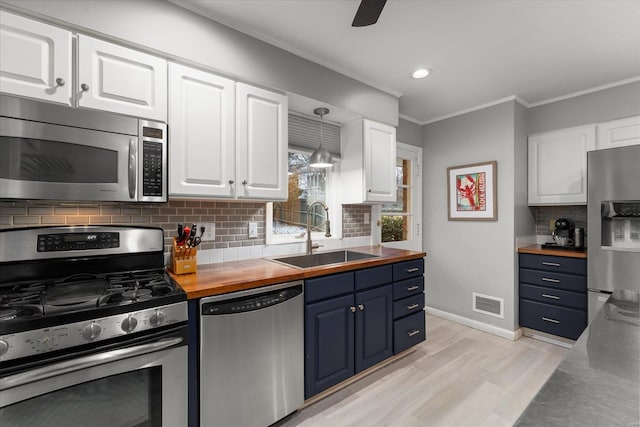 kitchen with wood counters, appliances with stainless steel finishes, sink, white cabinetry, and blue cabinetry