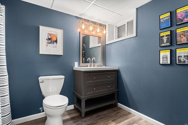 bathroom with toilet, hardwood / wood-style flooring, a drop ceiling, and vanity