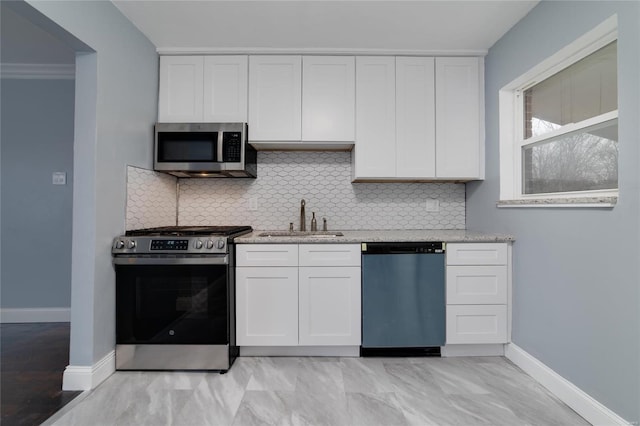 kitchen with appliances with stainless steel finishes, white cabinetry, a sink, and light stone countertops