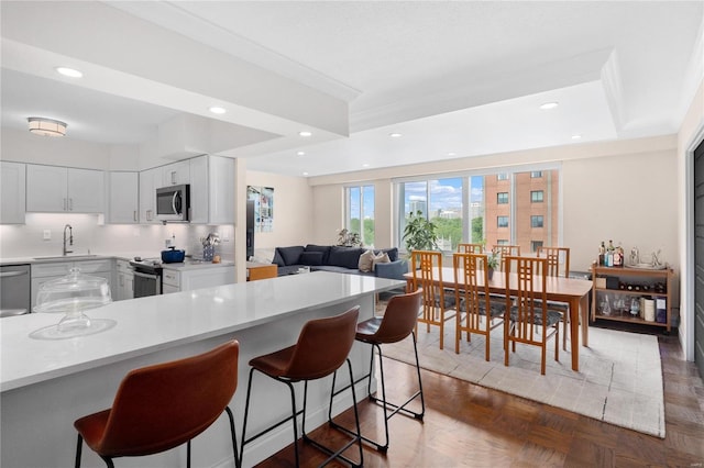 kitchen featuring a breakfast bar area, light countertops, decorative backsplash, appliances with stainless steel finishes, and a sink