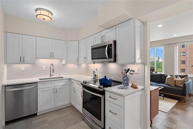 kitchen featuring appliances with stainless steel finishes, a sink, light countertops, white cabinetry, and backsplash