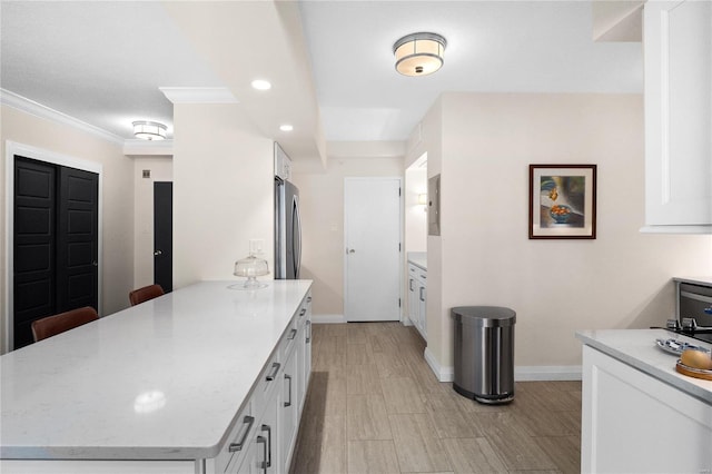 kitchen featuring baseboards, ornamental molding, freestanding refrigerator, light stone countertops, and white cabinetry