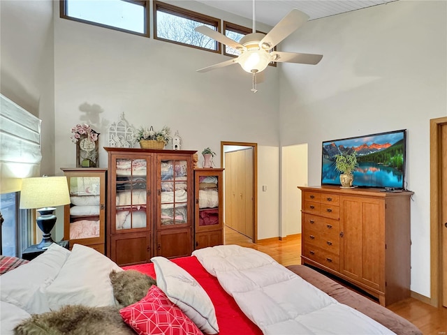 bedroom featuring light hardwood / wood-style flooring, ceiling fan, and a high ceiling