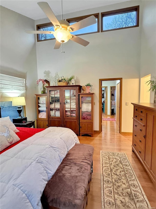 bedroom featuring ceiling fan, a towering ceiling, and light wood-type flooring