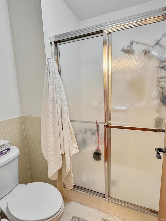 bathroom featuring walk in shower, toilet, tile patterned flooring, and tile walls