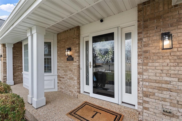 doorway to property with a porch and brick siding