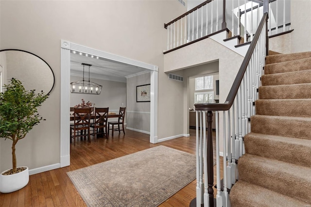 staircase featuring hardwood / wood-style floors, a towering ceiling, visible vents, and baseboards