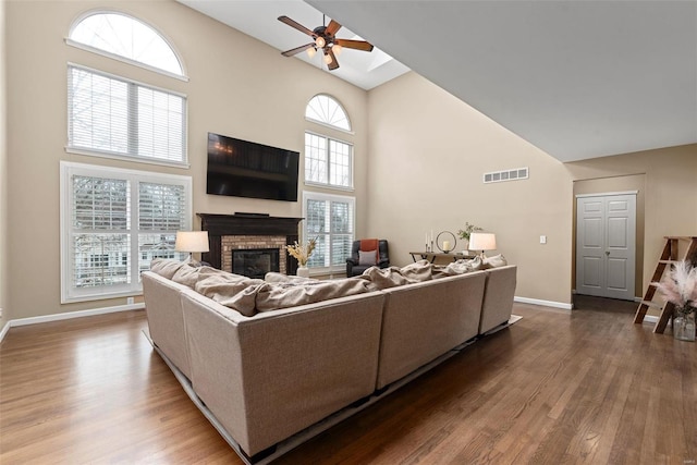 living room featuring visible vents, ceiling fan, wood finished floors, a high ceiling, and a fireplace