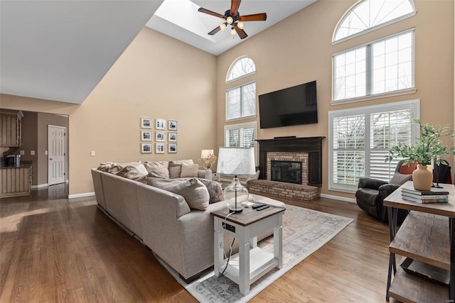 living area featuring baseboards, ceiling fan, wood finished floors, a high ceiling, and a fireplace