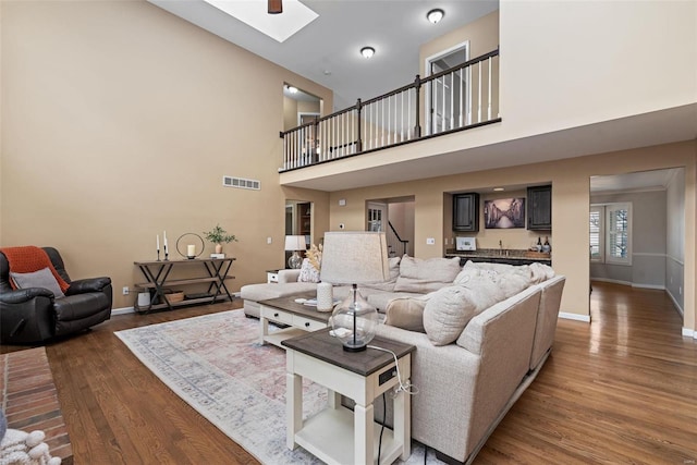 living area with a skylight, wood finished floors, visible vents, and baseboards