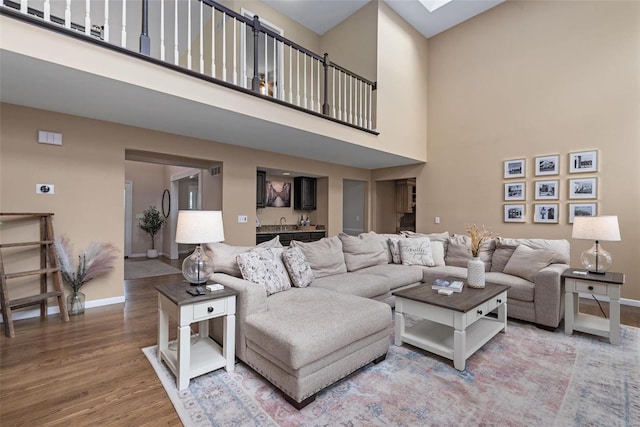 living area with a skylight, a high ceiling, baseboards, and wood finished floors