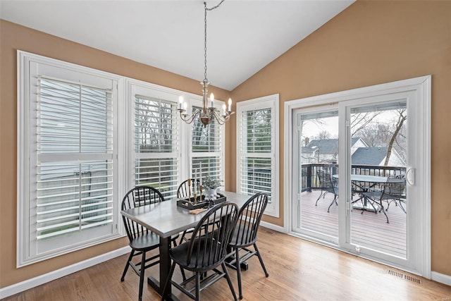 dining room with light wood finished floors, visible vents, baseboards, lofted ceiling, and a notable chandelier