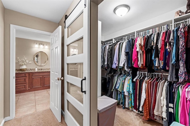 walk in closet featuring light tile patterned floors, a barn door, and light colored carpet