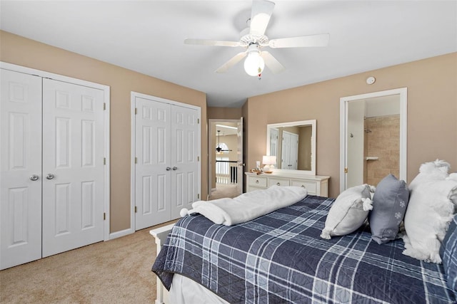 bedroom featuring multiple closets, light colored carpet, a ceiling fan, ensuite bath, and baseboards