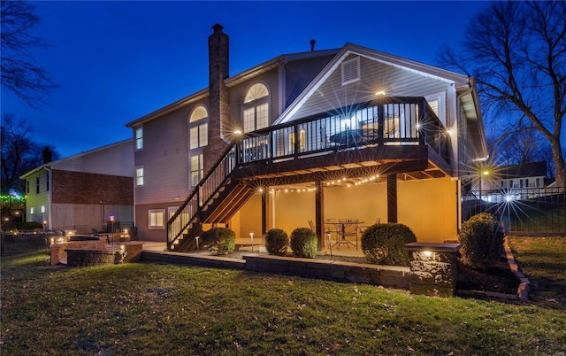 back of house at twilight with a chimney, a patio area, a lawn, and stairway