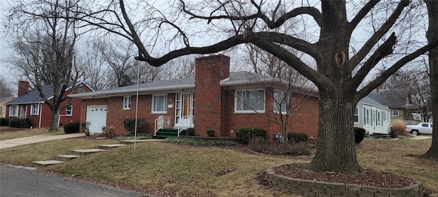 single story home featuring driveway, a chimney, a front lawn, a garage, and brick siding