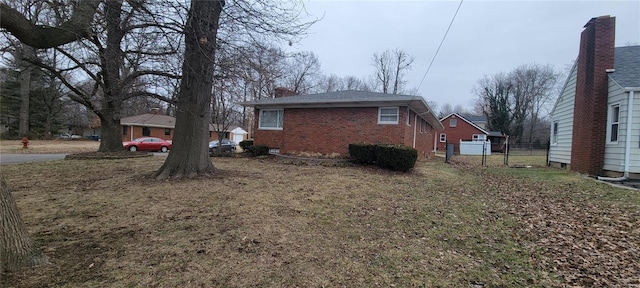 view of side of property with a yard, brick siding, and fence