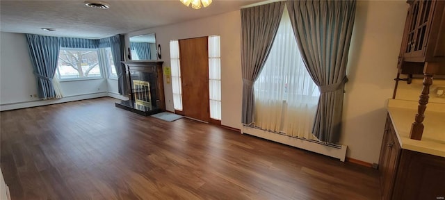 interior space featuring dark wood-style floors, visible vents, a fireplace with raised hearth, and a baseboard radiator