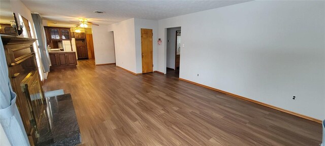 unfurnished living room featuring dark wood-style floors, a ceiling fan, and baseboards