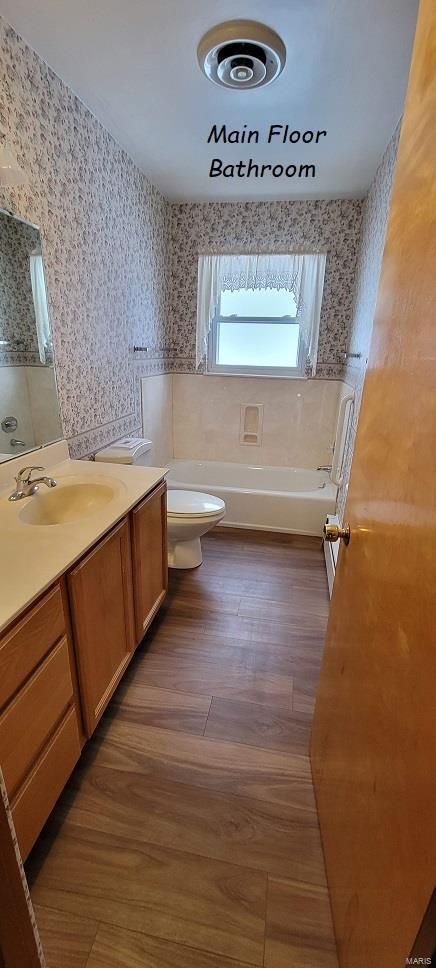 bathroom with vanity, wood finished floors, a tub to relax in, wallpapered walls, and toilet